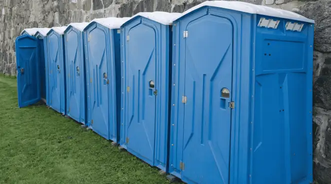 Row of blue portable toilets lined up on grass against a stone wall for event sanitation in New Orleans, LA
