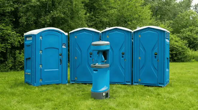 Four blue portable toilets and a matching hand washing station on grass near trees, a common sight at local outdoor events in New Orleans, LA